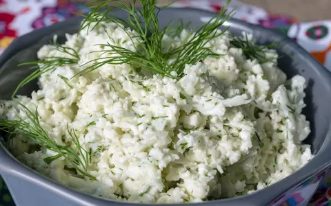 Pyszna surówka z kalafiora, posypana świeżym koperkiem, w szarej misce.