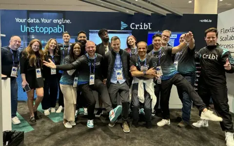 A lively group of Cribl customers and staff pose for a photo at a trade show, all smiles and team spirit.