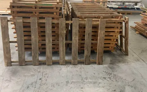 Des planches de bois recycle, issues de palettes, forment une barrière devant d'autres palettes empilées.