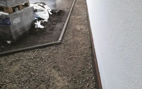 Wykonano opaskę wokół domu z kruszywa, obok ułożone palety z materiałami budowlanymi.