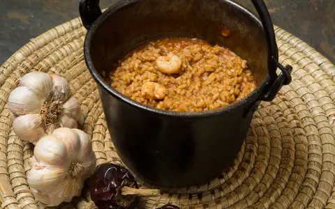 Caldero murciano humeante en olla de hierro, con gambas, ajos y pimientos secos.