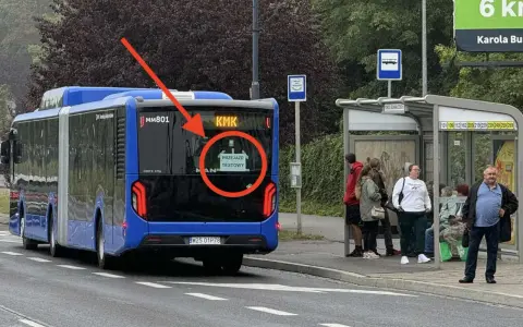 Niebieski autobus przegubowy z napisem "PRZEJAZD TESTOWY" na tyle, stoi przy przystanku autobusowym.