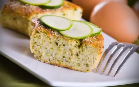 Saporito sformato di zucchine, guarnito con fette di zucchina fresca e una spolverata di parmigiano. Perfetto per un pasto leggero.