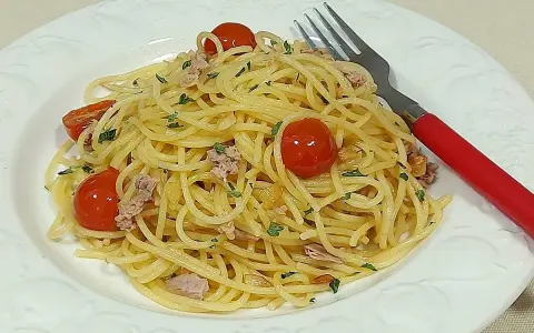Espaguetis al ajillo con tomates cherry y atún, servidos en plato blanco con tenedor rojo.