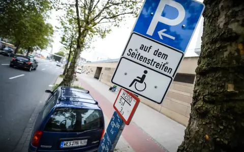Schild für Behindertenparkplatz auf dem Seitenstreifen. Falschparken wird mit einer hohen Strafe geahndet.