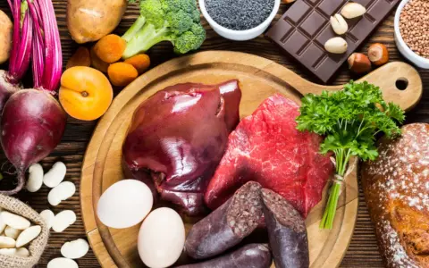 Eine Auswahl an eisenhaltigen Lebensmitteln: Rindfleisch, Leber, Blutwurst, Eier, Linsen, Rote Bete, Spinat, Brokkoli, Aprikosen, Schokolade und Vollkornbrot.