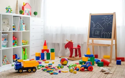 Kolorowy pokój zabaw dla dzieci w domu. Na dywanie rozrzucone klocki, ciężarówka, traktorek, huśtawka-łoś i tablica z rysunkiem domku.