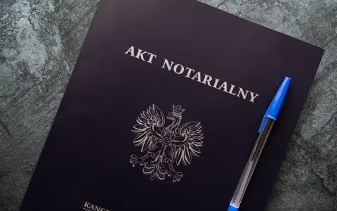 Na ciemnogranatowej okładce widnieje napis "AKT NOTARIALNY" i godło Polski. Obok leży niebieski długopis.
