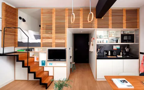Estudio moderno de piso 25 metros cuadrados con cama elevada, cocina compacta, zona de TV y escaleras de madera.