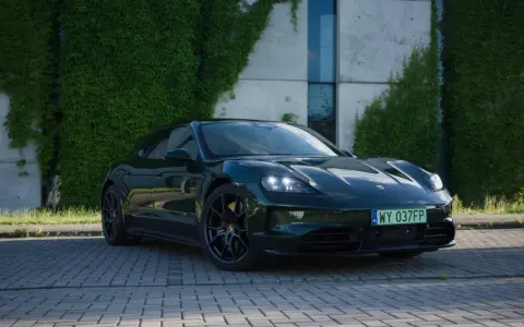 Elegancki, ciemnozielony Porsche Taycan na tle zielonej ściany z bluszczu. Sprawdź aktualną porsche taycan cena i możliwości tego elektrycznego cudu.