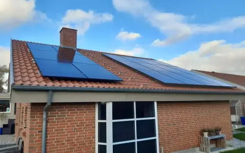 Ett tegelhus med solpaneler på taket, redo att generera egen energi. Blå himmel med vita moln.