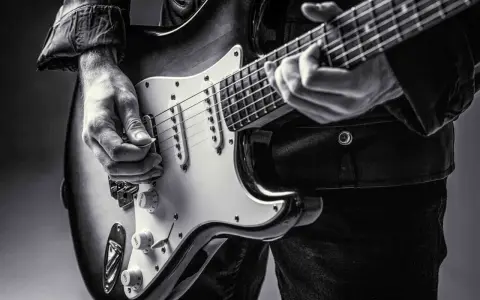 Ręce muzyka grające na gitarze do metalu. Czarno-białe ujęcie z bliska.