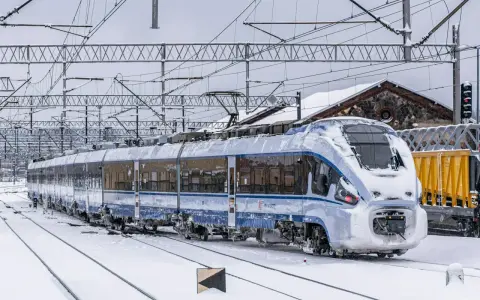Pociąg PKP Intercity pokryty lodem i śniegiem, stojący na zaśnieżonych torach. Utrudnienia w ruchu kolejowym z powodu zimy.