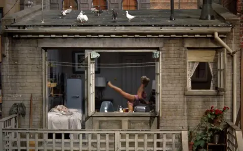 La trama de "La finestra sul cortile" si svela: una donna in lingerie fa ginnastica in un appartamento, mentre sul tetto i piccioni osservano.
