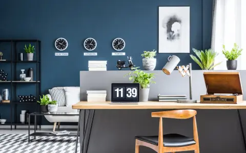 Biuro z zegarami pokazującymi czas w Nowym Jorku, Londynie i Tokio na ścianie w kolorze navy. Na biurku laptop, lampa i gramofon.