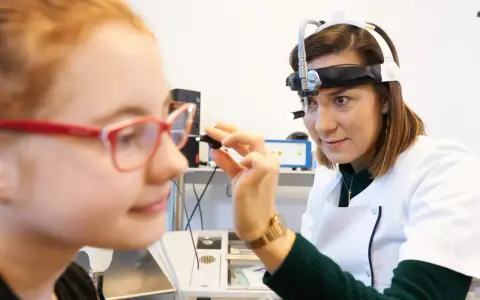 Lekarka bada ucho dziewczynki, która ma okulary. Badanie może pomóc zdiagnozować niedosłuch u dziecka.