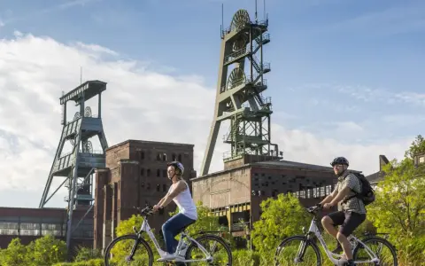 Zwei Radfahrer genießen die Landschaft am ehemaligen Bergwerk Ewald. Die imposanten Fördertürme stehen im Hintergrund.