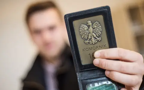Komornik pokazuje legitymację z orłem. W tle niewyraźna postać mężczyzny, być może w związku z długiem osób prywatnych.