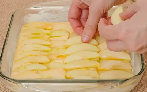 Ręce układają plasterki jabłek na cieście. Powstaje pyszne ciasto z jabłkami, gotowe do pieczenia.