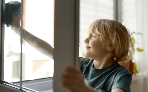 Chłopiec z uśmiechem na twarzy myje okno. To część jego listy obowiązków domowych dla dzieci.