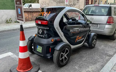 Czarny Renault Twizy z napisem "Free! for our guests" zaparkowany przed hotelem Petite Fleur. Obok znak parkingowy dla gości hotelowych.