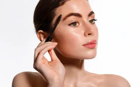 Une femme applique un mascara pour un maquillage des yeux parfait. Ses sourcils sont brossés et ses cils sont mis en valeur.