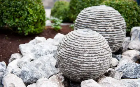 Dwie kamienne kule z betonu, przypominające ułożone krążki, stanowią element wodnej instalacji ogrodowej. Dowiedz się, jak zrobić kulę z betonu.