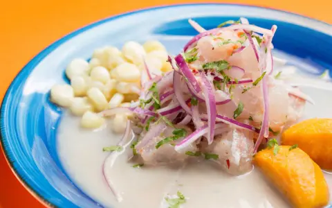 Ceviche frais baignant dans un leche de tigre crémeux, garni d'oignons rouges, de coriandre, de maïs et de patate douce.