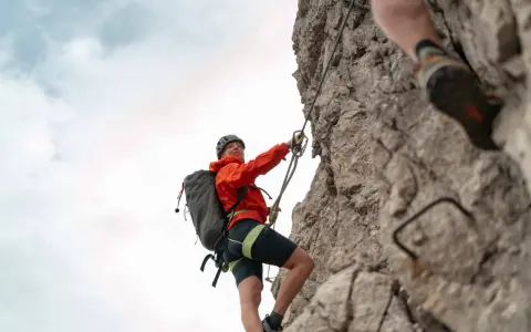 Kletterin im orangefarbenen Anzug sichert sich am Drahtseil des Alpspitz Klettersteigs. Ein spannendes Abenteuer in den Bergen.