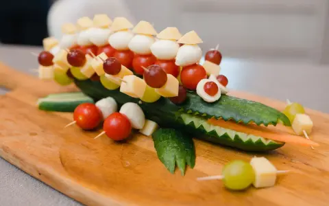 Krokodil aus Gurke mit herzhaftem Fingerfood für Kinder: Käse, Tomaten, Mozzarella & Trauben auf Spießen.
