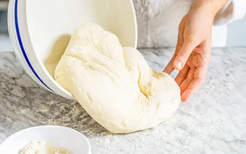 Frischer Teig, der aus einer Schüssel auf eine bemehlte Arbeitsfläche gleitet. Ähnlich wie Mehl Typ 0, ideal zum Backen.