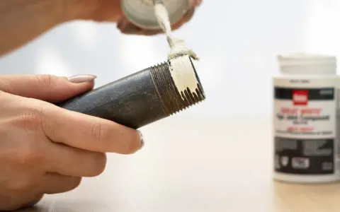 Application de pâte sur le filetage d'un **tube pour joint**. Un pot de pâte est visible à droite.