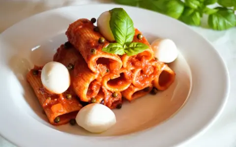 Rigatoni z sosem pomidorowym, kulkami mozzarelli i bazylią. Szybki obiad z makaronem z czerwonym pesto ze słoika.