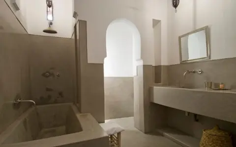 Modernes Badezimmer mit einer freistehenden Badewanne und einem Waschbecken aus Tadelakt. Ein großer Spiegel und ein traditioneller Korb vervollständigen den Look.