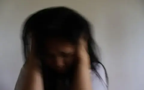Mujer con cabello oscuro, con las manos en la cabeza, rostro agachado. Expresión de angustia, quizás por la ansiedad antes de la regla.