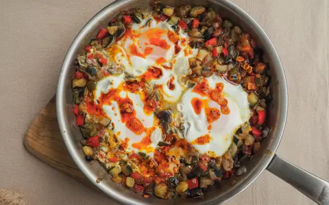 Huevos al plato con verduras salteadas, pimientos, calabacín y berenjena, todo en una sartén.