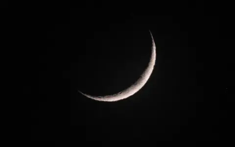 Eine schmale Mondsichel leuchtet im dunklen Nachthimmel. Sie erinnert an den Beginn von Ramadan, wann die Zeit des Fastens beginnt.