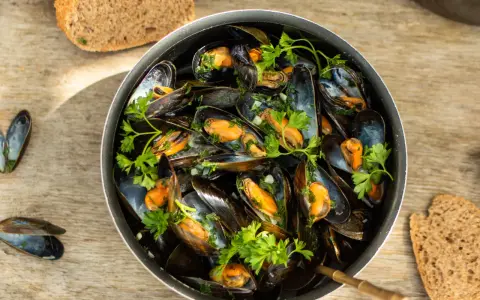 Un plat généreux de moules marinières, garni de persil frais, avec du pain de campagne à côté.