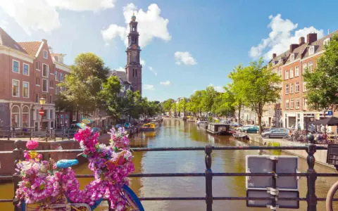 Das **beste von Amsterdam**: malerischer Kanal mit Booten, historischen Gebäuden und einem Kirchturm. Blumenverzierte Fahrräder auf einer Brücke.