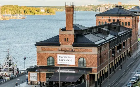 Fotografiska Stockholm vid vattnet, med en båt i förgrunden och en stadssilhuett i bakgrunden.