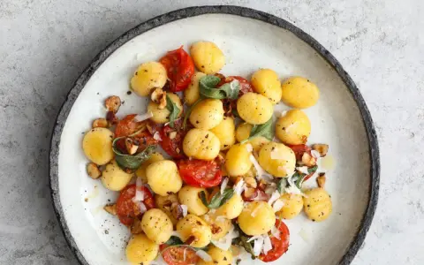 Gnocchi z pomidorkami koktajlowymi, szałwią i orzechami laskowymi, posypane parmezanem. Pyszne danie na obiad.