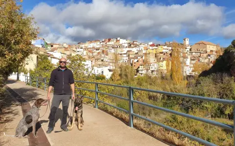 Hombre paseando con dos perros por la ruta de las esculturas de Bogarra, con el pueblo al fondo.