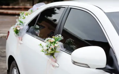 Biały samochód ozdobiony bukietami kwiatów na klamkach i błotniku.