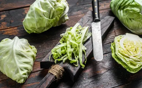 Frischer spitzkohl schneiden für einen Salat. Ein Messer liegt neben dem geschnittenen Kohl auf einem Holzbrett.