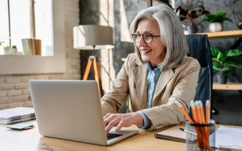 Femme souriante travaillant sur son ordinateur portable, planifiant sa future pension pré cheval.