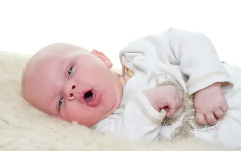 Baby mit offenem Mund, vielleicht husten. Was tun? Ein süßer kleiner Mensch auf weichem Fell.