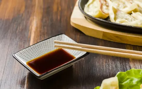 Sos sojowy w miseczce z pałeczkami, obok pierożków gyoza. Szukasz alternatywy, czym zastąpić sos sojowy?
