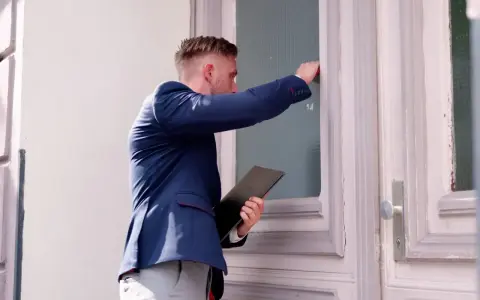 Mężczyzna w garniturze puka do drzwi, trzymając teczkę. Zastanawia się, ile zabierze komornik z premii.