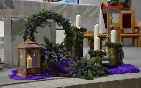 Piękny adwentowy wystrój w kościele: wieniec z gałązek, świece i fioletowe ozdoby. Dekoracje adwentowe tworzą uroczysty nastrój.