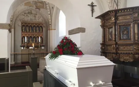Biała trumna z czerwonymi różami w kościele. Warto wiedzieć, jak się zachować przy otwartej trumnie, by okazać szacunek zmarłemu.
